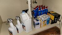 Photo showing Bona cleaning spray bottles and large jug, Clorox bleach toilet cleaner bottles, boxed light bulbs, and skewer grill set box on shelf.