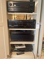 White shelving unit holding four black AV components and a remote control on bottom shelf