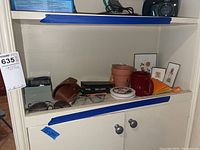 Shelf with sunglasses, reading glasses, poker card set, shot glasses, small framed art, wallet, and other small items.