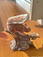 Red squirrel figurine poised on branch with white flower, detailed view.