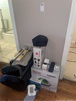Foot massagers, blood pressure monitors with cuffs, personal cooling system, massage tool box, and small accessories grouped on hardwood floor against wall.