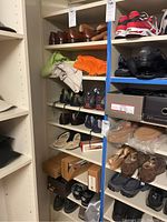 Shelves filled with various men's shoes including leather dress shoes, running sneakers, casual shoes, slippers, and some folded men's clothing items such as shorts or pants, plus footwear boxes.