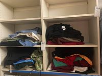 Shelving with folded men's clothing items in various stacks including shorts, t-shirts, polo shirts, and sweaters in assorted colors