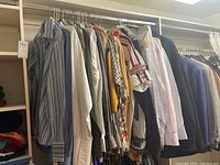 Wide view of all hanging men's shirts and coat including striped, solid, and patterned shirts and a sports coat