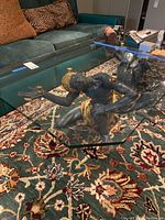 Glass coffee table on patterned rug with focus on one ceramic figure supporting glass top.