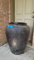 Photo showing the large pottery planter vase with etched texture near a door on concrete surface.