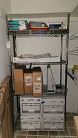 Full front view of metal shelving loaded with office storage boxes and supplies, showing wire shelves and chrome poles.