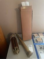 Photo of telescope, wooden tripod and cardboard box placed on table.