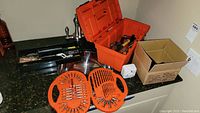 Orange Black and Decker tool box open showing compartments with drill bits, screwdriver bits, sockets and accessories on a granite countertop.