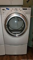 Front view of white Whirlpool Duet dryer mounted on pedestal showing overall appearance.