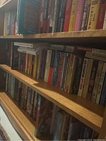 Books arranged on wooden shelves showing a mix of paperback and hardcover books with visible titles including fiction and nonfiction.