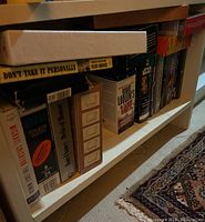 Photo showing a shelf with multiple books on tape cassette cases, titles visible including 'Don't Take It Personally', 'The Last Worthy', 'Desert Gold', 'Robert Ludlum's The Apocalypse Watch'