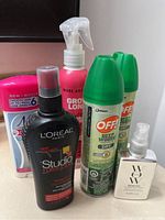 Six personal care items arranged on a counter including Nair sensitive hair remover lotion, L'Oréal Studio Line hair spray, Marc Anthony Grow Long spray, two OFF! Deep Woods insect repellent spray cans, and a small NYVO Dreamy Aura spray bottle.