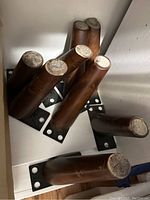 Eight cylindrical wooden furniture legs with dark brown finish and metal mounting plates, arranged in a box.
