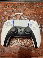 Top view of white and black PS5 DualSense controller showing symmetrical analog sticks, face buttons, and central touchpad with blue LED light bar active.
