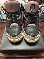 Front view showing black leather upper, grey tongues with red Jumpman logo, black laces and elephant print toe box detail.