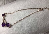 Top angle of bracelet showing pear cut purple amethysts, white cubic zirconia, and rose gold plated chain on white background.