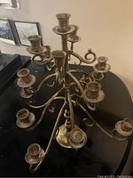 Photo of multi-arm brass candleholder with multiple candle cups, visible tarnish and patina.
