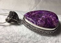 Close-up of pear-shaped purple Charoite stone pendant set in silver with ornate bail