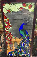 Front view of stained glass panel showing peacock perched on balustrade with foliage.