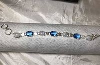 Full length photo of the silver bracelet with alternating oval moonstones and blue topaz stones on a white cushion.