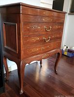 Closed view of solid wood silverware chest with brass inlay and handles, showing front and side with decorative gold stencil and curved legs.
