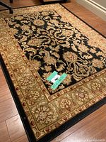 Full view of rectangular black and beige floral patterned area rug on hardwood floor