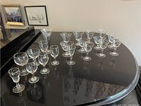Photo showing multiple clear glass stemware pieces of various sizes arranged on a black surface including etched floral pattern glasses.