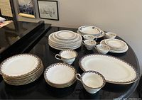 Photo showing multiple china plates, cups, saucers and serving items from the Tuscan and other sets on a round black table.