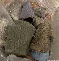 Close-up photo of yarn spools in a bag, showing green, tan, and purple colors.