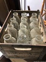 Overview of wooden crate filled with 12 clear glass milk bottles, seen from top.