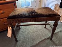 Front and side view of the wooden framed cushioned vanity bench showing the worn brown fabric and carved apron detail