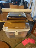 Stack of picture frames and cardboard pieces on a table, plastic tub with books underneath