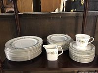 Photo showing stacked large dinner plates, smaller plates, a creamer, and a cup with saucer, all with floral pattern and gold trim.