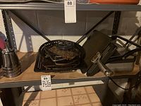 Photo showing various used metal cooking pans and a black Cuisinart panini press with metal handles on a shelf.