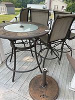 High top round patio table and four swivel armchairs on outdoor deck, umbrella stand base visible in foreground.