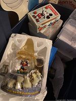 Close-up of Mickey Mouse snow globe inside styrofoam packaging showing detailed top hat and white dove figures around base