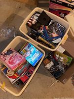 Bins filled with assorted DVDs, Blu-rays and some household items alongside a cardboard box containing dishes and silverware.