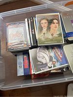 Plastic bin filled with DVDs and Blu-ray cases on hardwood floor