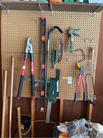 Photo showing various gardening tools including long handled shovel, pruners, a level, soil scoop, shears, and cultivator hung on pegboard