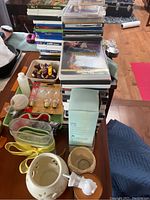 Photo showing stacked kids' DVDs, toy figures, light bulbs in packaging, various small items including candle holders and twine on table.