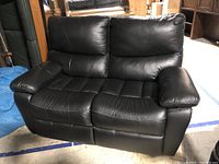 Front view of the black leather loveseat showing two separate seats, cushioned armrests, and stitched black leather upholstery.