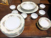 Full view of Noritake dinner set with stacked plates, cups with saucers, serving bowl and dish on wooden surface