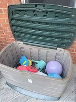 Open plastic outdoor storage bin showing balls, frisbees, watering can, and paneling inside