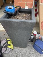 Dark gray square tapered planter showing soil residue inside and surrounding items.