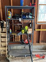 Full view of metal shelving unit with tools placed on shelves including two chainsaws, pole saw, and safety items