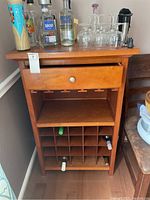 Front view of the wooden wine cabinet showing the drawer, open shelf, and bottle grid storage with some wine bottles stored inside.