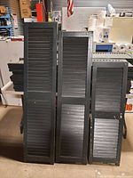 Photo of three individual upright wooden slatted shutters of varying heights with dark paint and visible wear