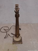 Full view of the ornate brass table lamp showing the vertical column body, socket at top, and power cord.