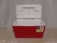 Front view of red and white Coleman cooler with the lid open showing the interior and label on the front.